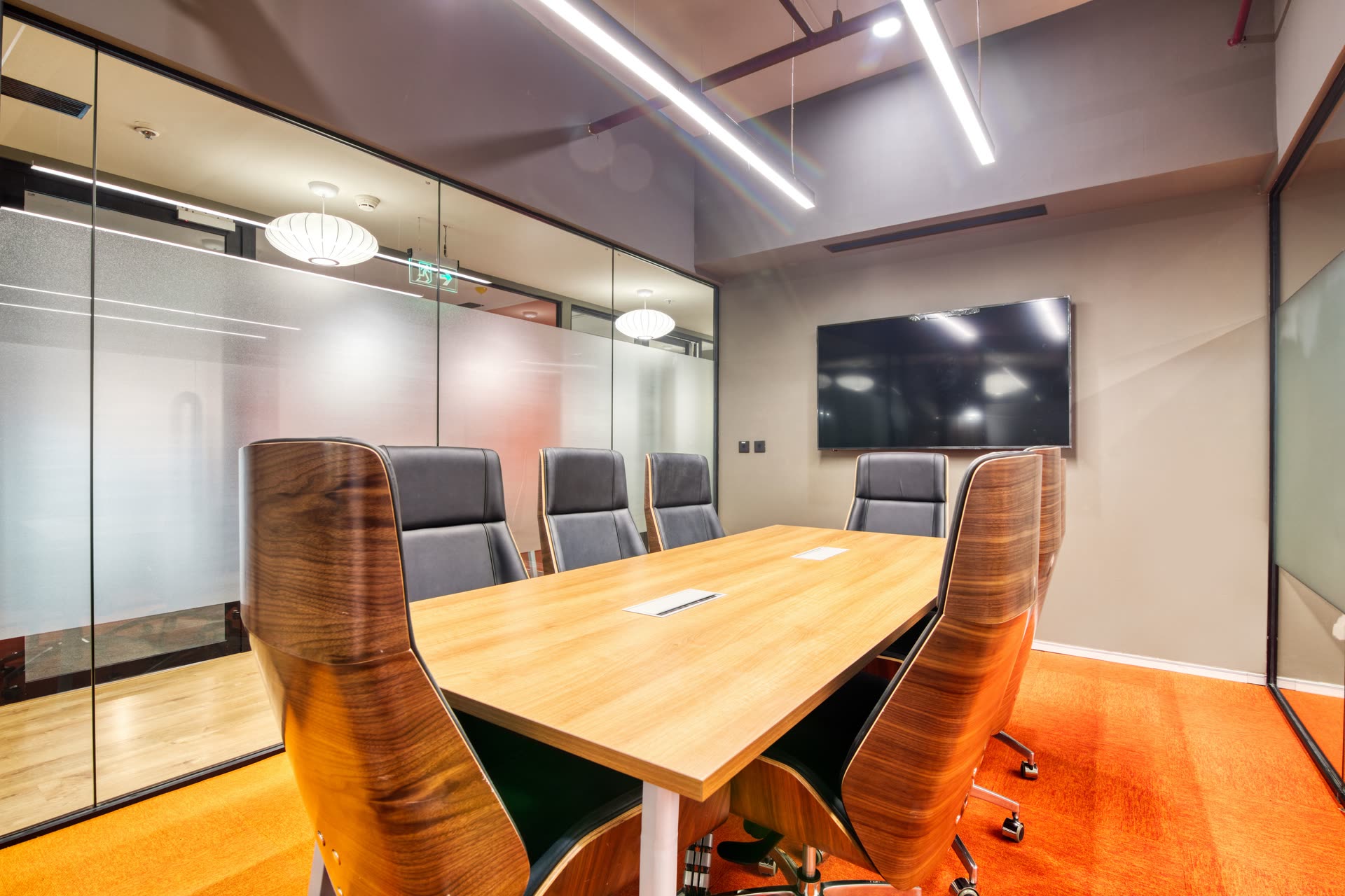 An empty meeting room with a wooden table, grey chairs and glass walls.