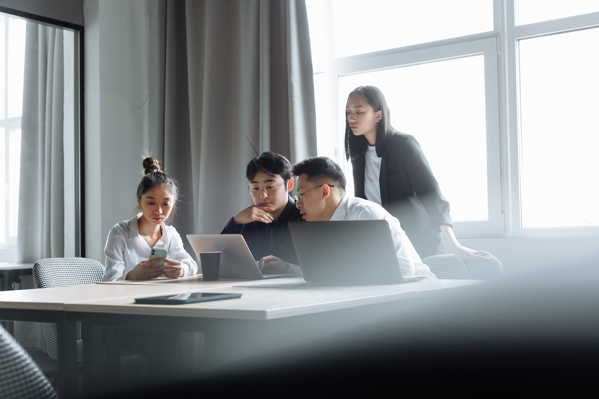 Young professionals working together at laptops by a large window in a bright office.
