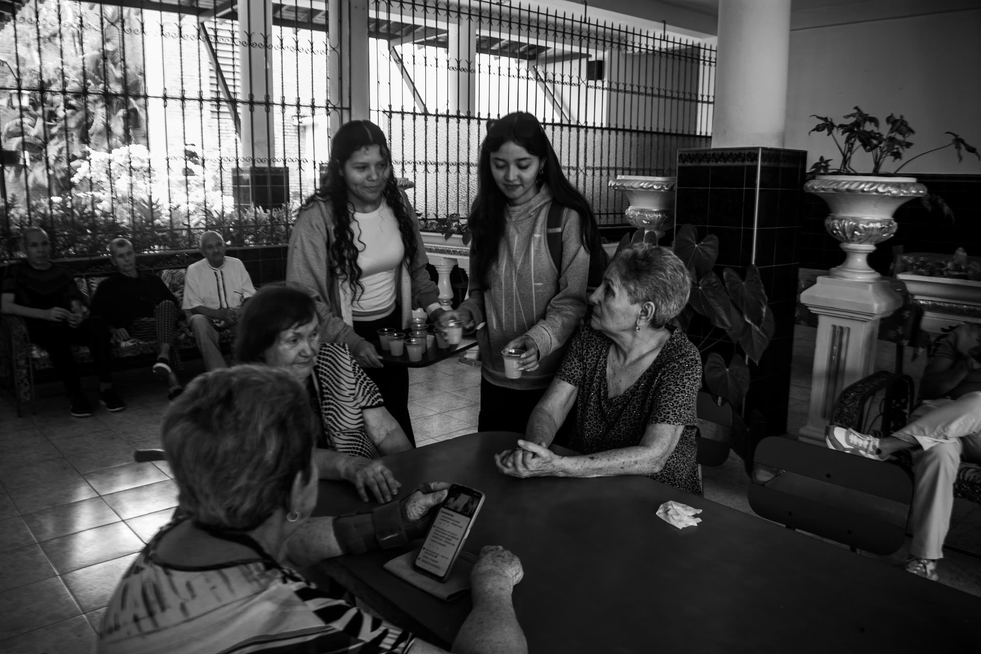 People of different ages talking around tables in a community space, in black and white.